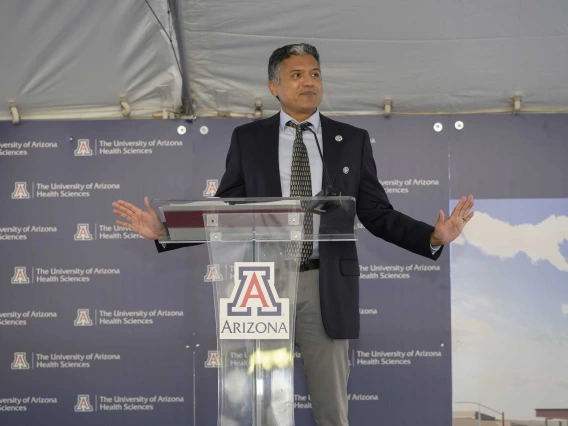 Deepta Bhattacharya, PhD, inaugural executive director of CAMI and a professor of immunobiology at the U of A College of Medicine – Tucson, wearing a dark suit, stands behind a clear lectern with the U of A logo on it.  