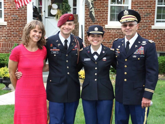 A family stands together with the father, son and daughter all in dress military uniforms while the mom is in a red dress. 