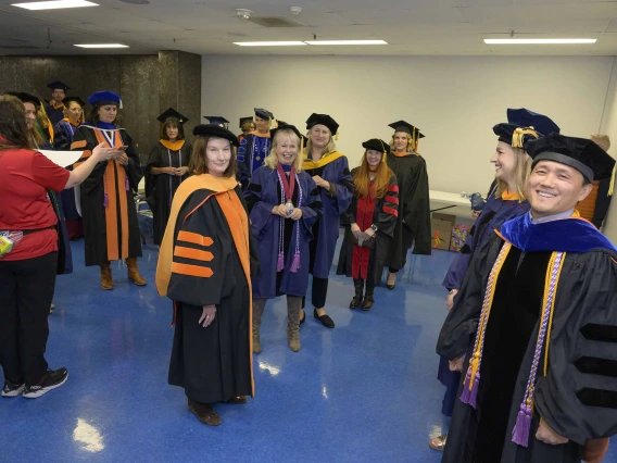 More than a dozen University of Arizona College of Nursing faculty and staff members dressed in graduation regalia smile as they line up in a room.
