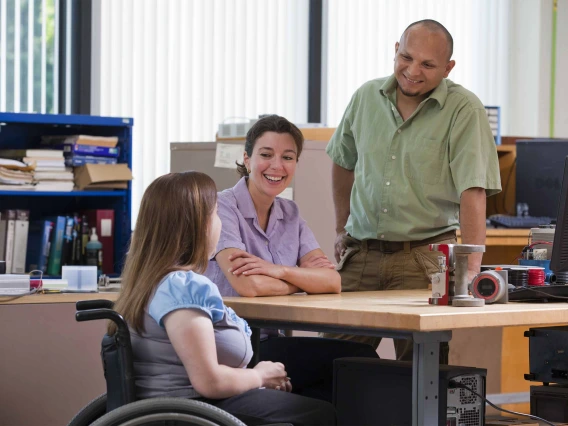 A person in a wheelchair chats with a two people in an office environment