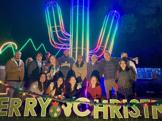 A group of people poses in front of a 15-foot saguaro lit up by LED lights.