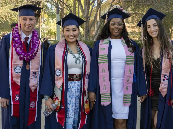 Four University of Arizona Mel and Enid Zuckerman College of Public Health students stand together wearing graduation caps and gowns.  