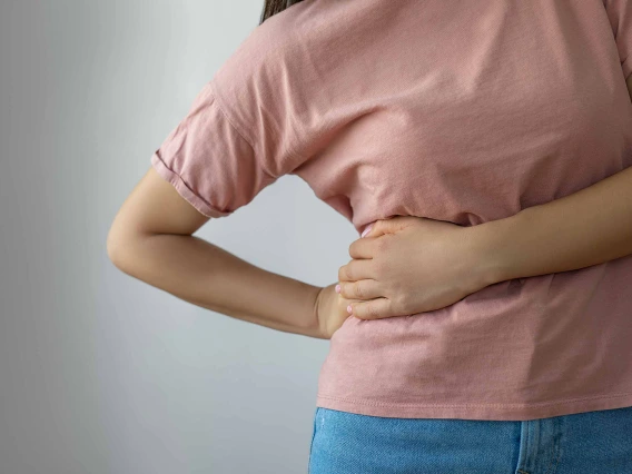 A woman grabs at the right side of her torso with both hands in a gesture of pain.