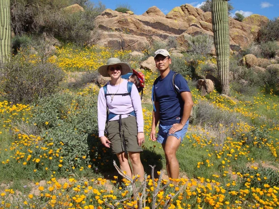 A couple with a baby in a carrier poses for a photo while hiking in the Sonoran Desert