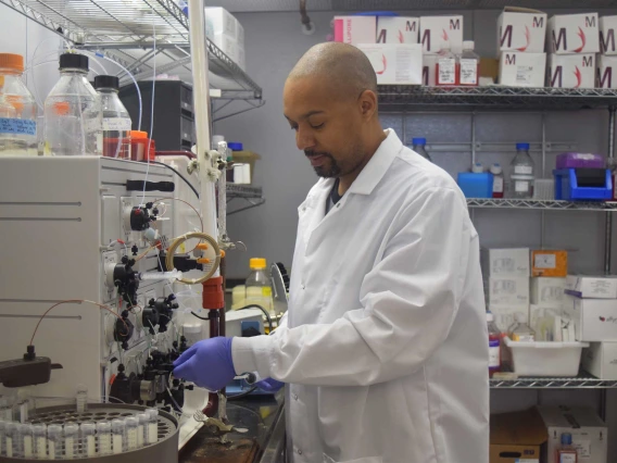 University of Arizona Health Sciences researcher Michael Johnson, dressed in a lab coat and wearing purple gloves, turns knobs on a piece of equipment.