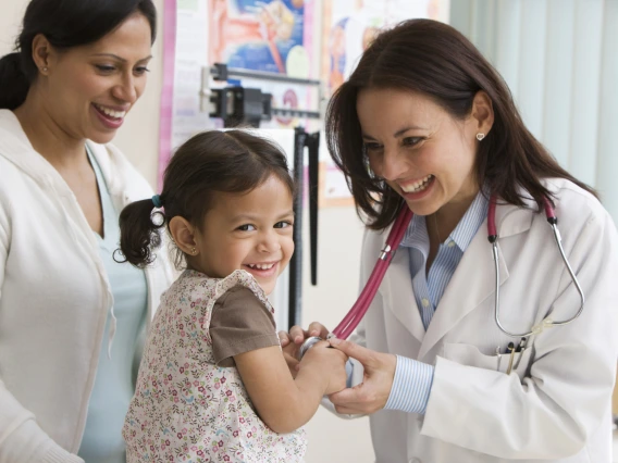 smiling doctor examines young child, laughing, while mother smiles in background