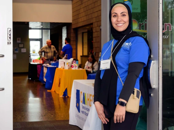 Arizona AHEC Scholar Diyana Ahmad smiles and holds the door open for people to enter community health clinic in Apache Junction, Arizona  