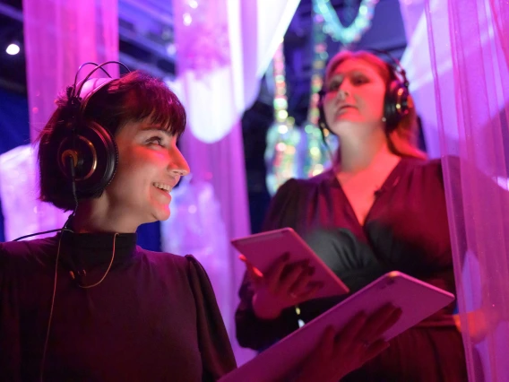 Two singers wearing headphones and reading music on a tablet