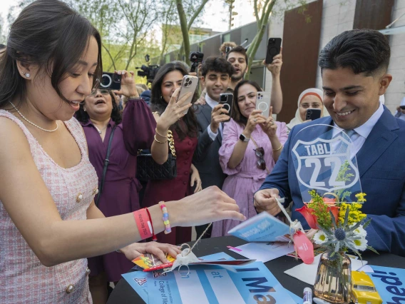 Two well-dressed medical students open envelopes while several family members stand around them with phones in the air taking photos and videos.  