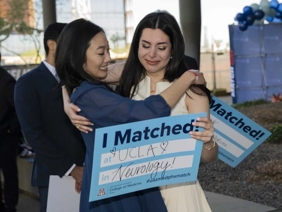 Two young women hug and smile as they hold signs that read, “I matched!”