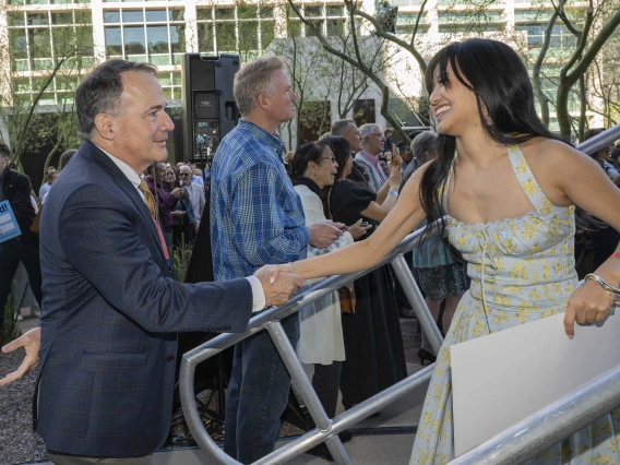 A young woman in a dress descends metal steps as she shakes hands with a man in a suit. 