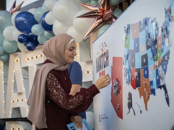 A woman wearing a hijab faces a map of the United States as she prepares to put a pin on the state of Arizona. 