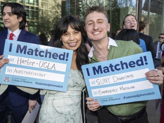 A woman and man both smile as they hold up signs that read, “I Matched!”