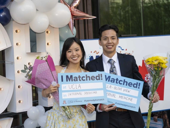 A woman and man both smile as they hold up signs that read, “I Matched!”