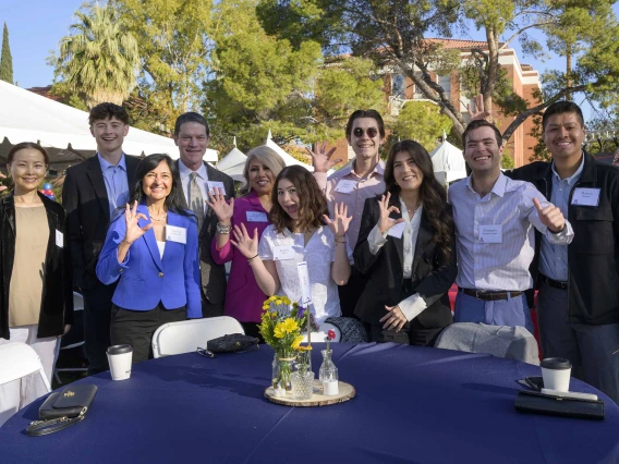 A group of about 10 students and faculty members stand outside behind a table, smiling and making the Arizona Wildcats hand sign. 