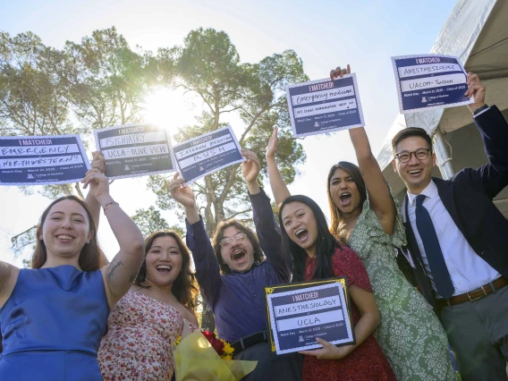 Six medical students smile and cheer as they hold up signs that read, “I matched!” in an outdoor setting. 