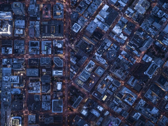 A city’s buildings, streets and neighborhoods glow at dusk, as seen from hundreds of feet in the sky. 