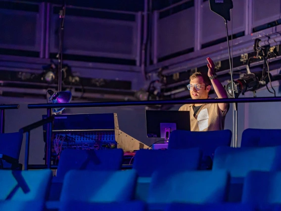 Person conducting singers from a sound booth in the searing area at the Tornabene Theater