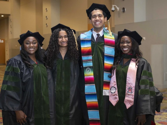 Four medical students stand together, smiling, in their graduation caps and gowns. 