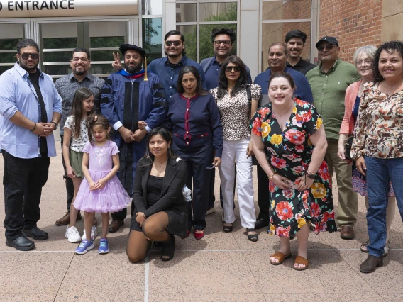 A graduate wearing a cap and gown stands in the middle of over a dozen family members of all ages. 