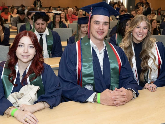 Several students in graduation caps and gowns sit in a room, smiling. 