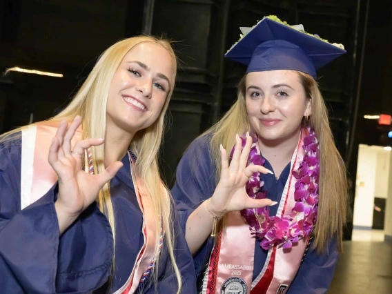 Two young women in graduation regalia smile and give the Arizona Wildcats hand sign.