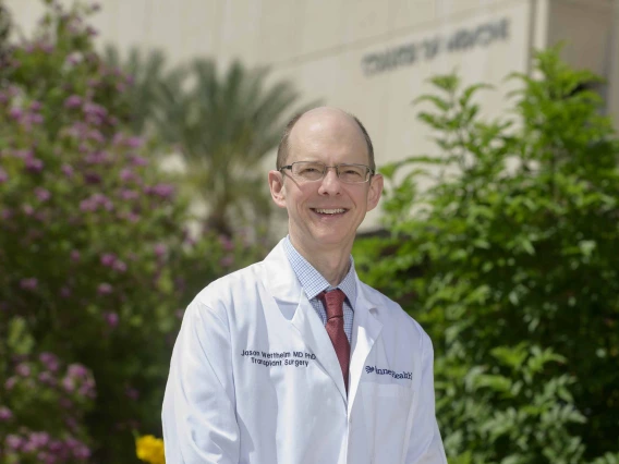 Portrait of Jason Wertheim, MD, PhD, in a white doctor’s coat standing outside. 