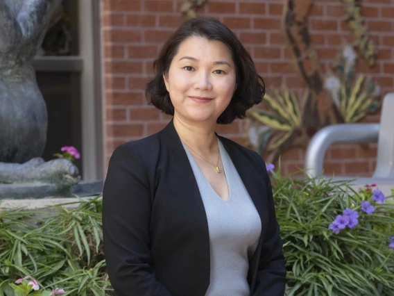 Portrait of Silvia Xu standing outside in front of some flowers and a brick building. 