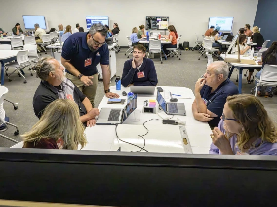 Onicio Leal Neto, PhD, MPH, stands at a desk next to a table full of people with laptops open in front of them.