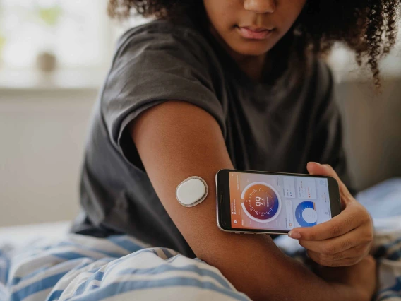 Young adult connecting smartphone to continuous glucose monitor, checking blood glucose