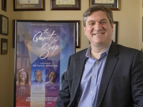 Portrait of Michael Grandner in front of a wall lined with framed photos and certificates.
