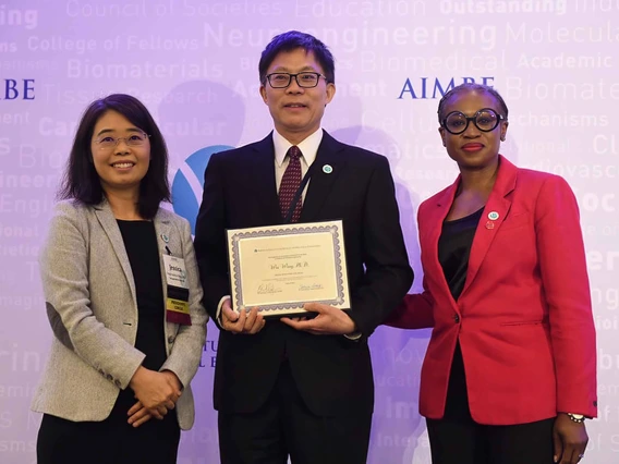 Professor Wei Wang stands between two women while holding a certificate. 