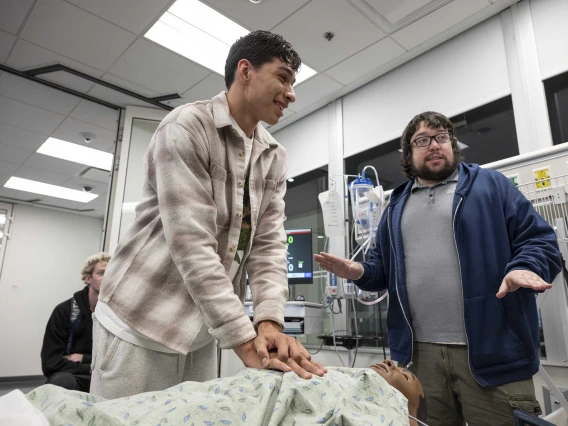 A high school student practices chest compression on a manikin while an instructor offers advice. 