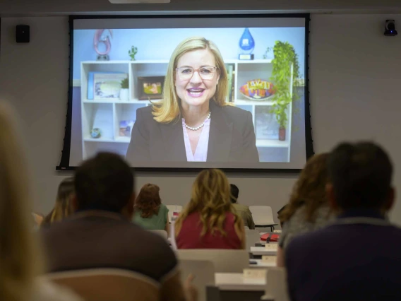 A large projector screen in a spacious conference room at the Phoenix Bioscience Core displays a recorded video message from Phoenix Mayor Kate Gallego, addressing rows of seated educators. 