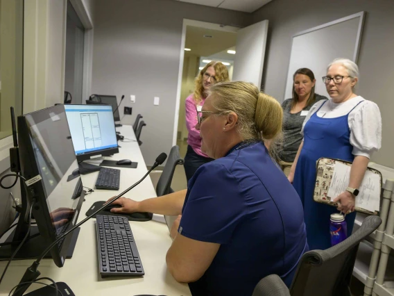 A woman sits at a control desk with multiple monitors and controls in the Center for Simulation and Innovation at the University of Arizona College of Medicine – Phoenix, managing a health care simulation.