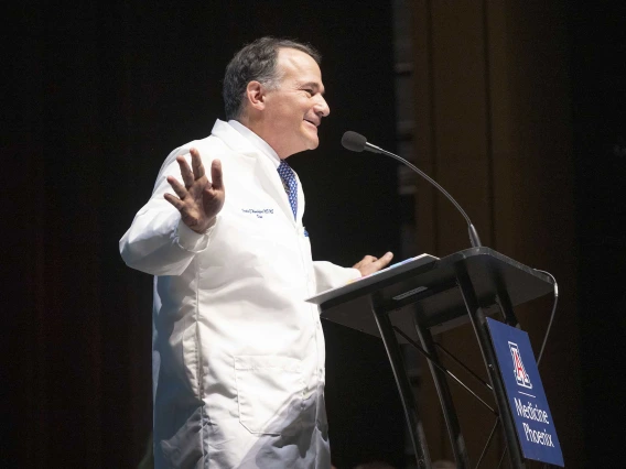 Fred E. Wondisford, MD, MS, MBA, speaks at a lectern while wearing a medical white coat. 