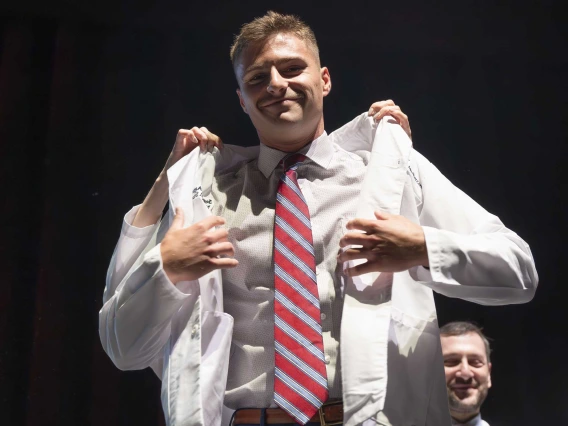 A medical student puts on his white coat with the help of a professor who is behind him. 