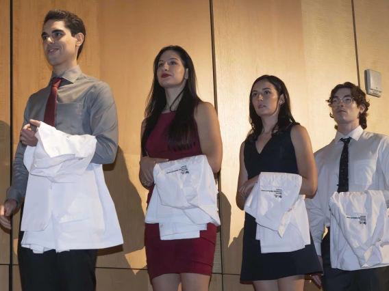 Four University of Arizona College of Medicine – Phoenix students stand in a line with medical white coats draped over their arms. 