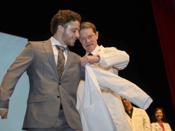 A new medical student smiles as a professor helps him put on his white coat.