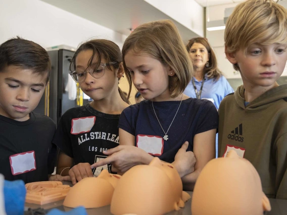 Four elementary students look at silicone faces on a table. 