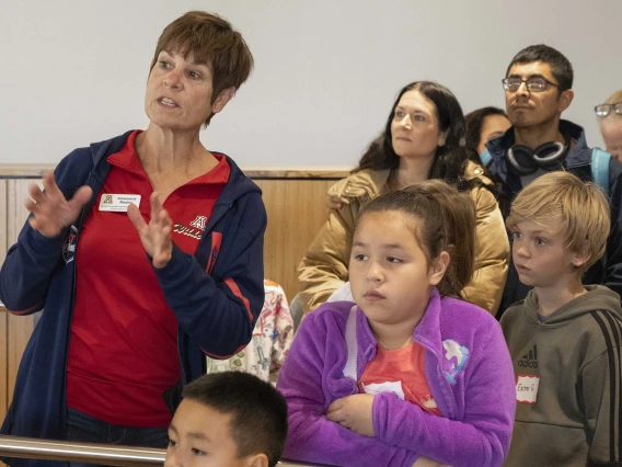 A woman in a red University of Arizona shirt talks to a group of elementary students. 