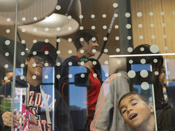 Two young boys make faces through a glass wall as their class walks through a building. 