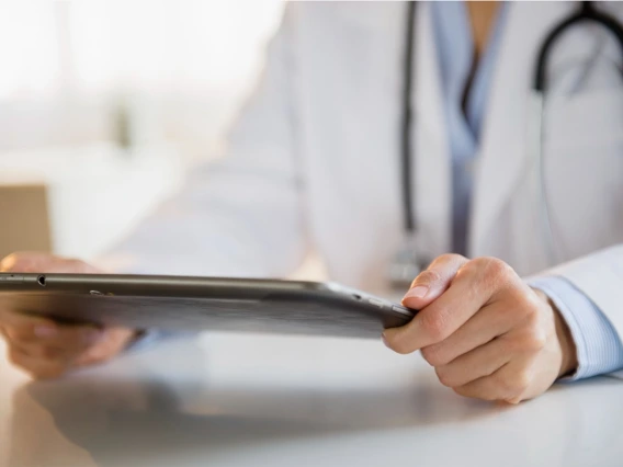 close up of doctor wearing white coat and stethoscope around neck holding an ipad