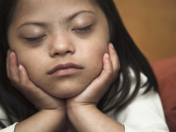 A girl with eyes closed and her chin resting in her hands