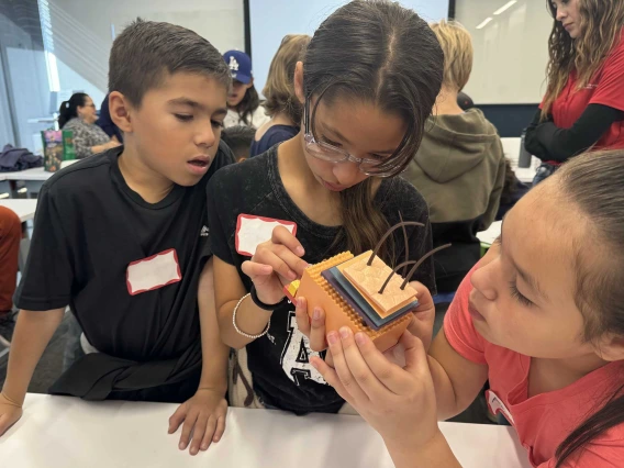 Elementary students stand around a table assembling a 3-D puzzle of the layers of human skin. 
