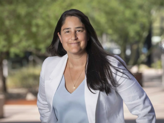 Portrait of Maya Kaelberer wearing a white blazer in an outdoor setting with trees in the background