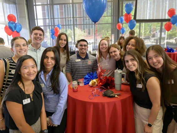 Several people look at the camera smiling with red and blue balloons in the background.