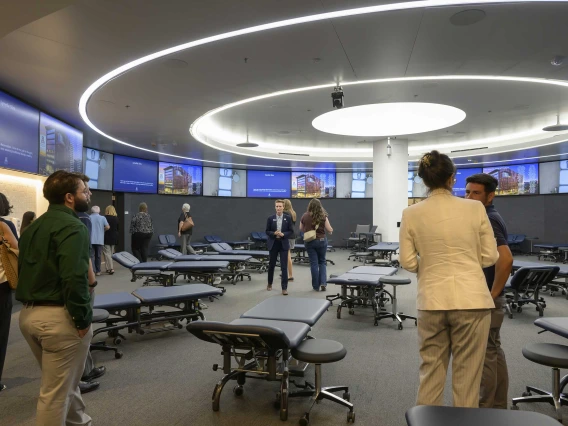 Photo of several people chatting together in a circular room filled with examining tables in the new lab space of the University of Arizona School of Health Professions Physical Therapy and Physician Assistant studios.