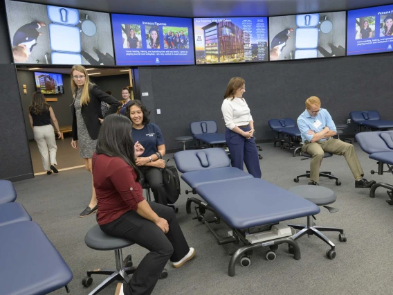 Several people sit near treatment tables while screens are lit up in the background.