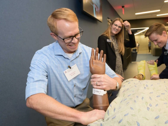 A man grasps the wrist of a simulation manikin dressed in a hospital gown.